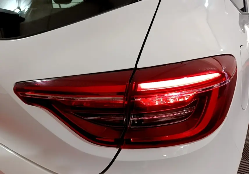 Gros plan sur le feu arrière droit rouge allumé d’une Renault Clio Business blanche, vue de trois quarts arrière.