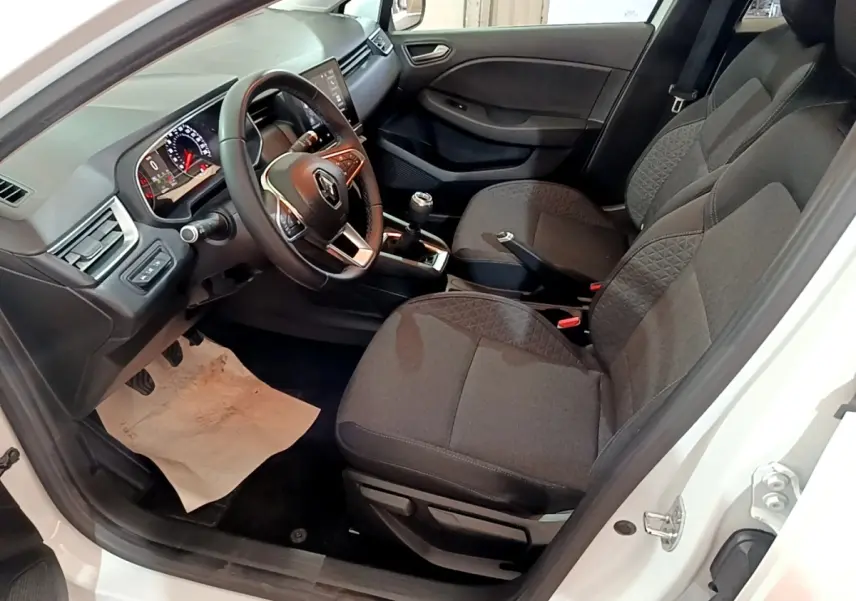 Vue intérieure côté conducteur de la Renault Clio Business blanche, avec volant cuir, tableau de bord numérique et sièges tissu gris.