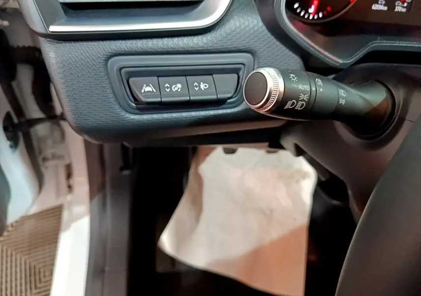 Vue intérieure rapprochée côté gauche du tableau de bord de la Renault Clio blanche, avec commandes d’aide à la conduite et commodo des phares.