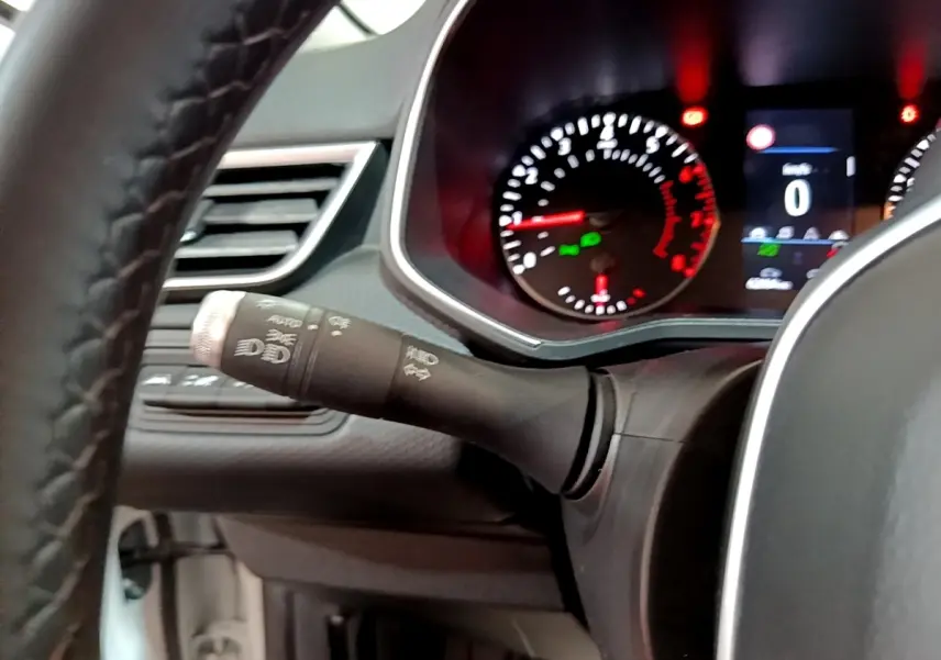 Intérieur Renault Clio blanc 2021, vue sur le tableau de bord avec compte-tours et commandes des phares sur la gauche du volant.