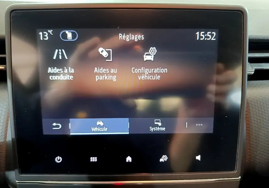 Écran tactile central du tableau de bord de la Renault Clio Business blanc, affichant les réglages d’aide à la conduite et parking.