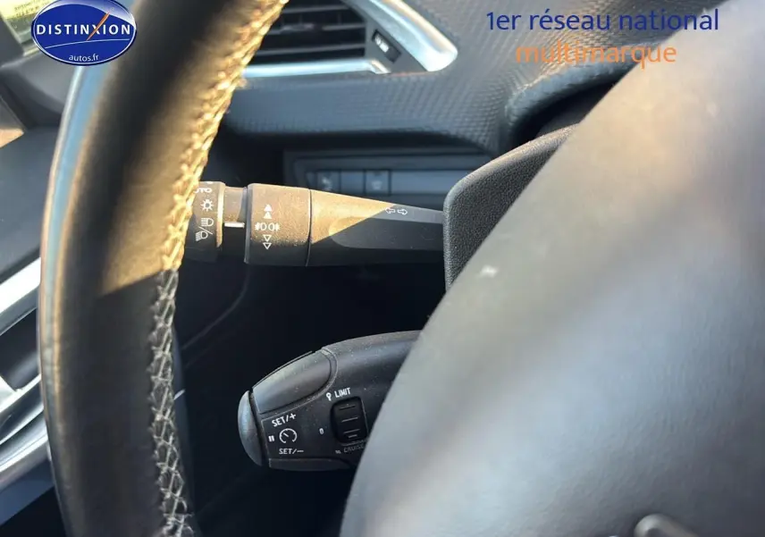 Gros plan sur le volant cuir multifonction du Peugeot 2008 gris clair, avec commandes de régulateur et clignotants visibles.