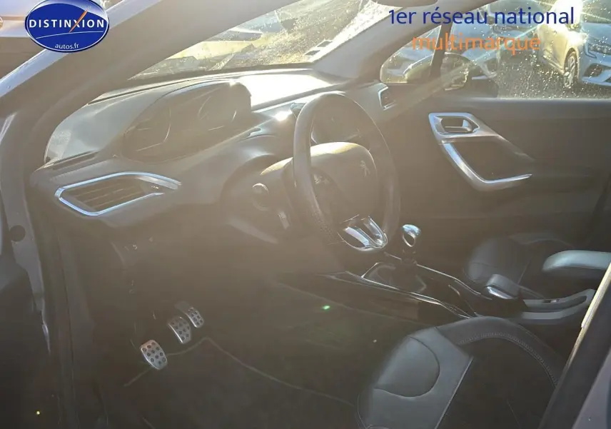 Vue intérieure côté conducteur du Peugeot 2008 gris clair, mettant en valeur le volant cuir et la boîte manuelle.
