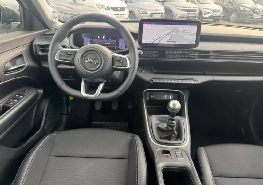 Vue intérieure avant du Jeep Avenger 2025 montrant le volant, la boîte manuelle et l'écran tactile de navigation.