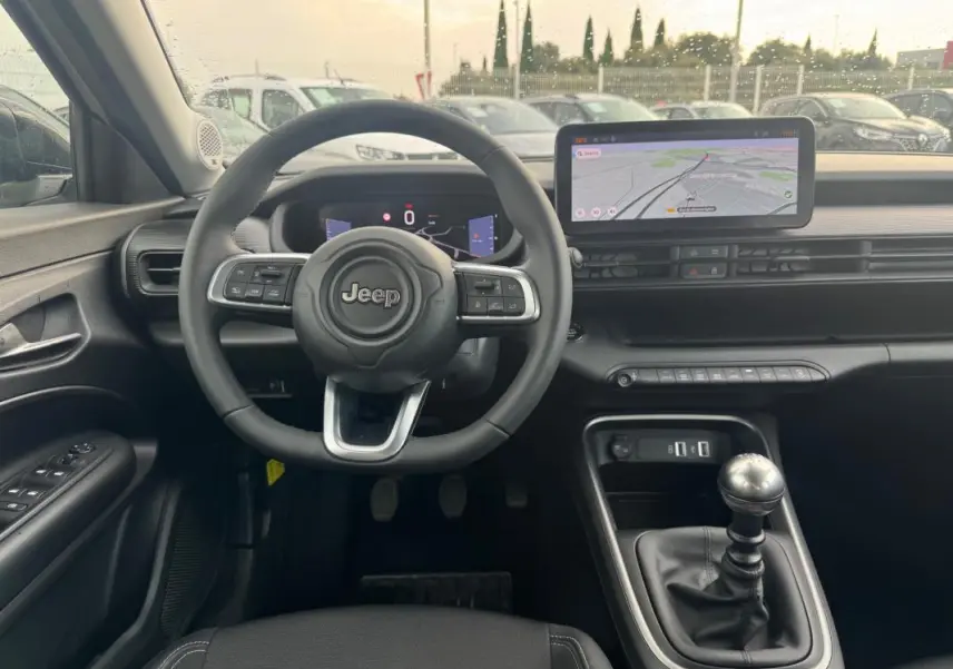 Vue intérieure avant du Jeep Avenger blanc 2025, volant multifonction, écran tactile et levier de vitesse manuel visibles.