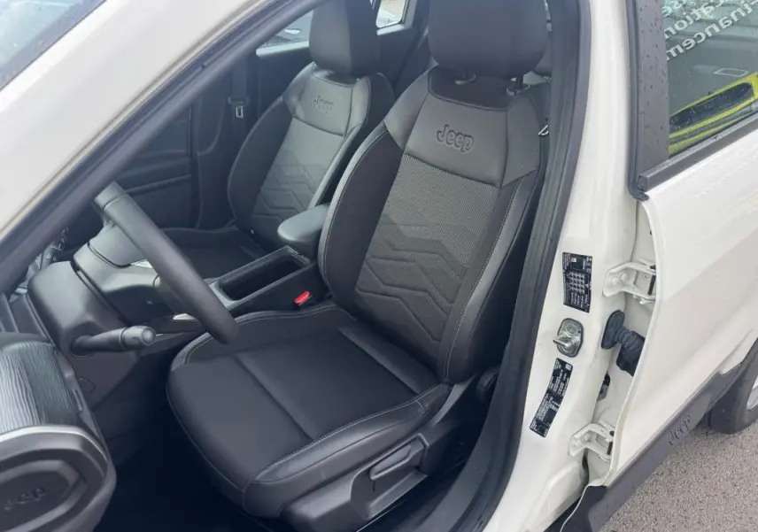Vue intérieure côté conducteur du Jeep Avenger blanc 2025, mettant en valeur les sièges noirs avec logo Jeep embossé.