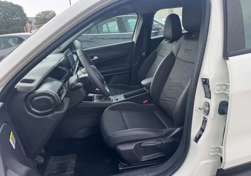 Intérieur avant droit du Jeep Avenger blanc 2025, sièges noirs avec logo Jeep brodé, volant et console centrale visibles.