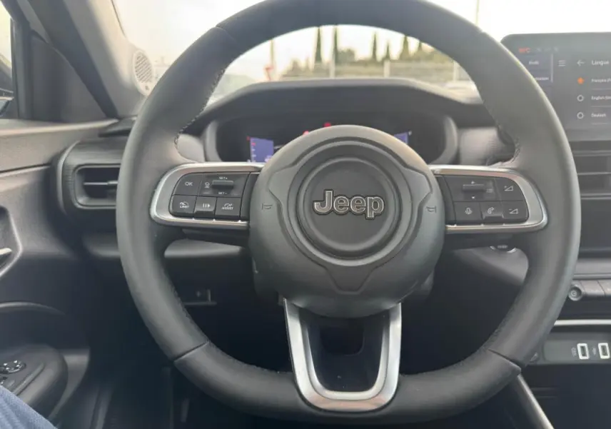 Vue intérieure centrée sur le volant noir du Jeep Avenger 2025 avec commandes multifonctions et tableau de bord numérique.