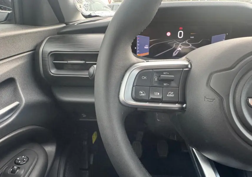 Vue intérieure centrée sur le volant et le tableau de bord numérique du Jeep Avenger blanc, avec commandes au volant visibles.