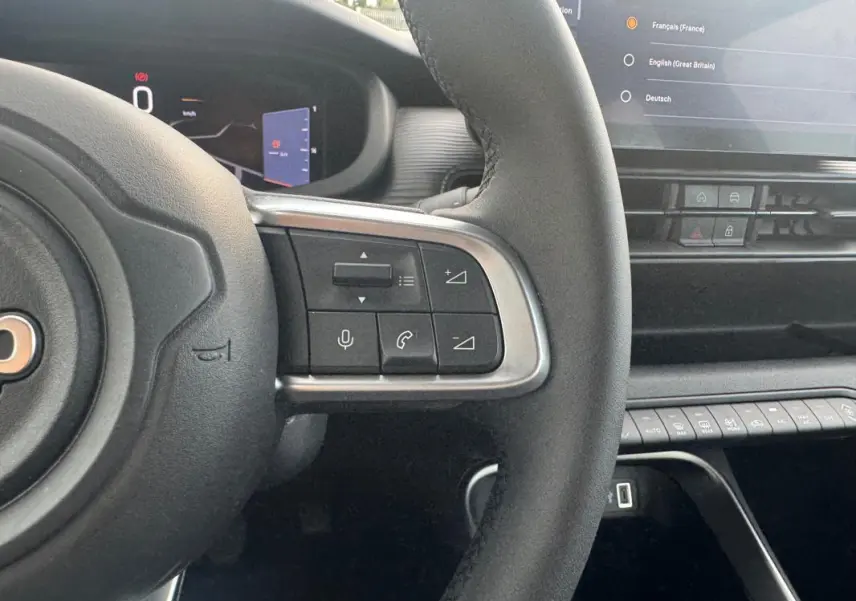 Vue rapprochée du volant à droite avec commandes intégrées et partie du tableau de bord numérique du Jeep Avenger blanc 2025.