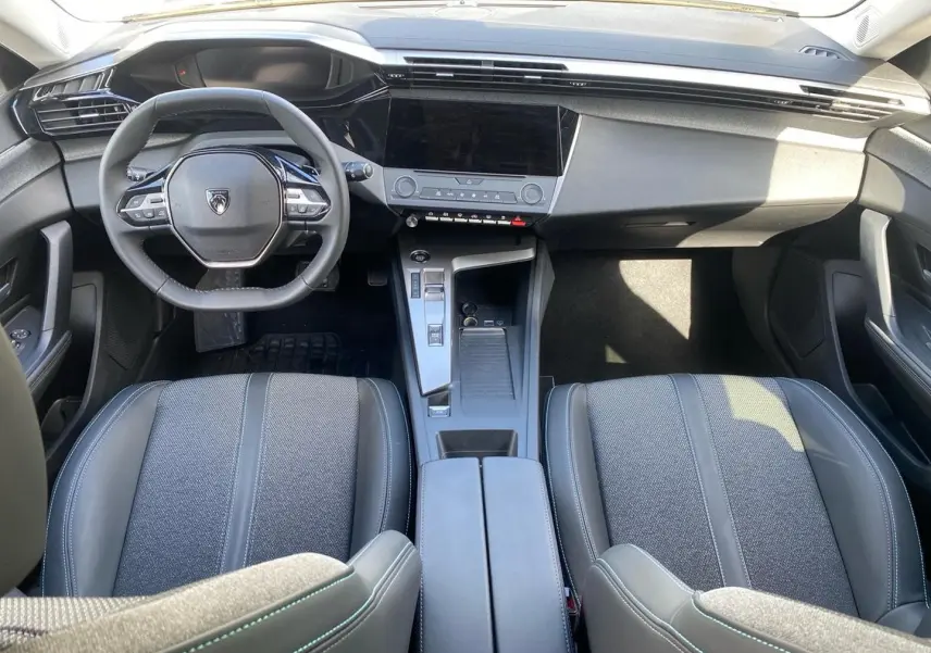 Vue intérieure avant de la Peugeot 308 2025 gris, montrant le volant multifonction, écran tactile et console centrale moderne.