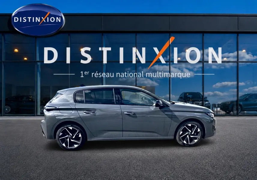 Profil droit d'une Peugeot 308 gris métallisé 2025 avec jantes alliage noires et blanches, devant un showroom Distinxion.