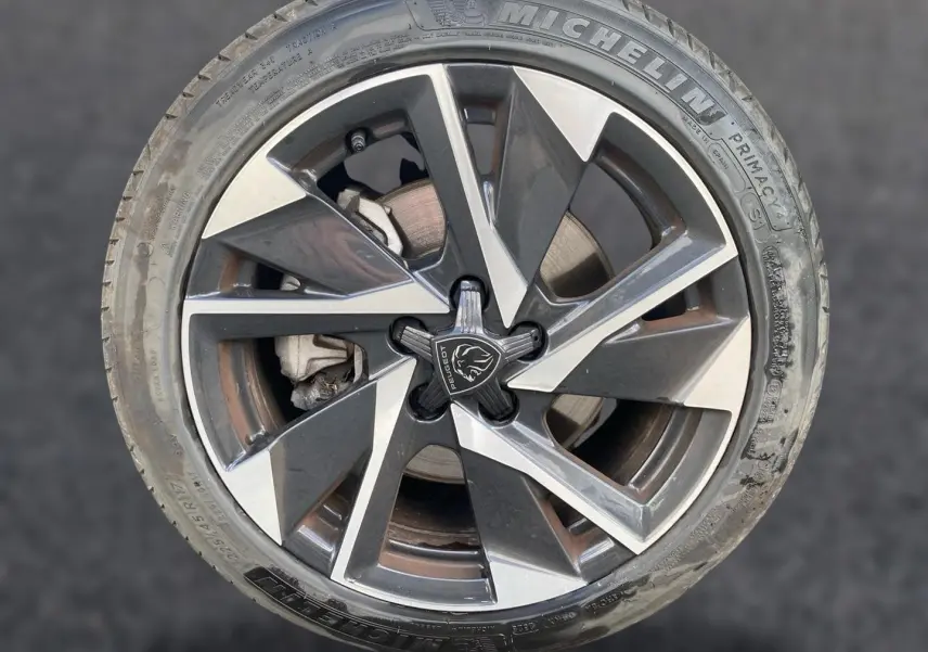 Gros plan sur la jante alu bicolore avec logo Peugeot au centre, montée sur pneu Michelin gris.