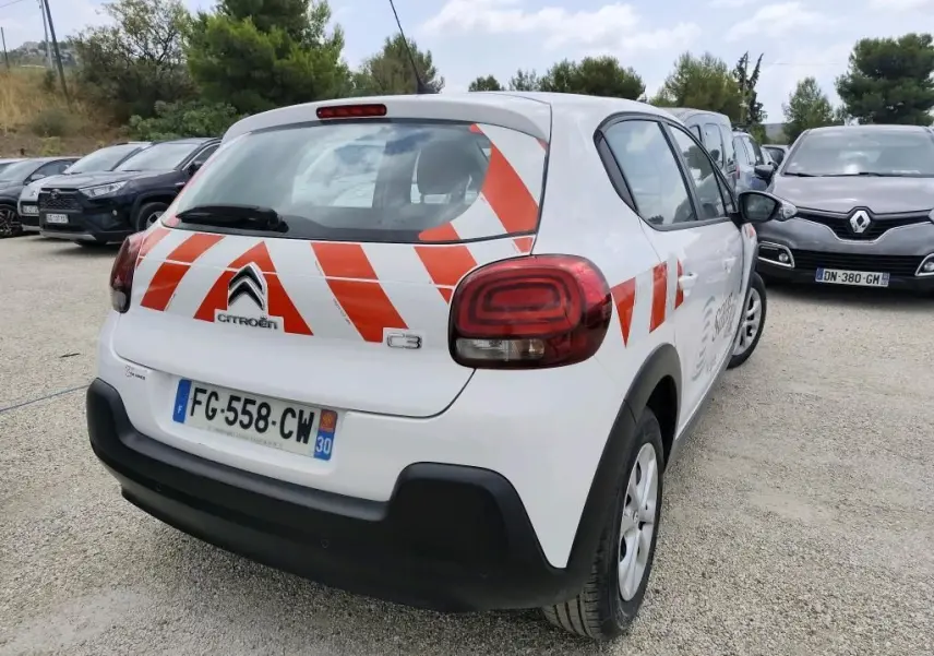 Vue 3/4 arrière droite d'une Citroën C3 Société blanche avec bandes rouges diagonales sur le hayon et le côté.