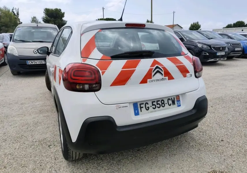 Vue 3/4 arrière droite d'une Citroën C3 Société blanche avec bandes rouges réfléchissantes diagonales sur le hayon.