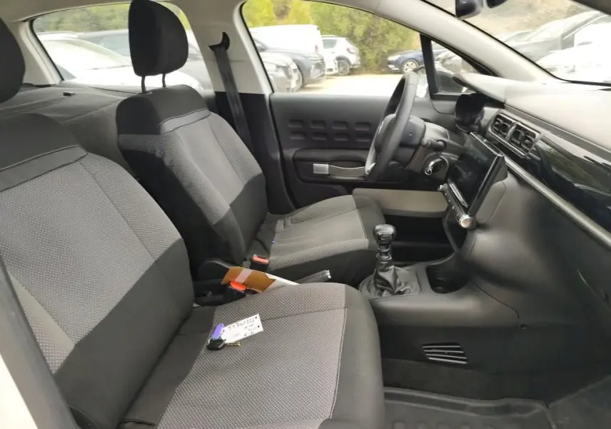 Vue intérieure côté conducteur de la Citroën C3 Société blanche, montrant les sièges tissu gris et la console avec boîte manuelle.