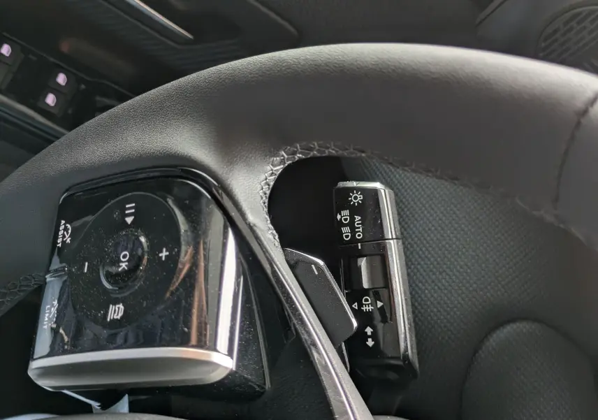 Gros plan sur le volant et la commande d’éclairage du Citroën C5 Aircross hybride, intérieur noir texturé.