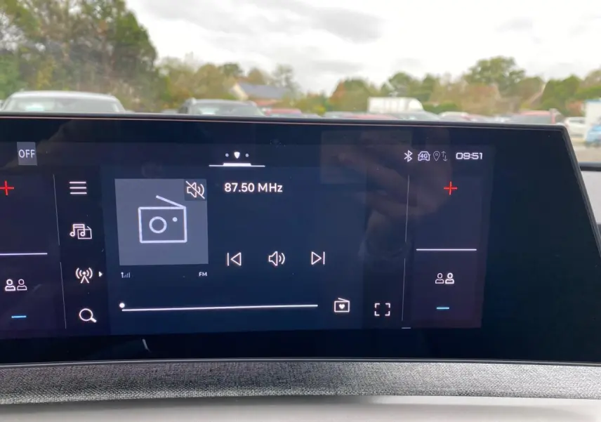 Écran tactile du tableau de bord du Peugeot 3008 Hybrid 2026 affichant la radio FM à 87,50 MHz en extérieur flou.