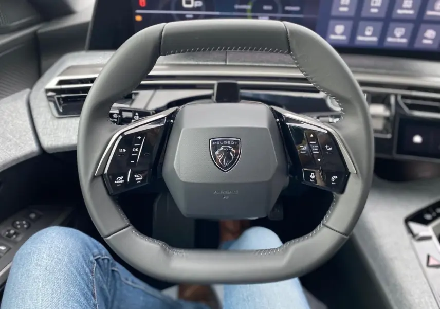 Vue rapprochée du volant cuir noir du Peugeot 3008 2026 avec logo lion et commandes intégrées, tableau de bord numérique en arrière-plan.