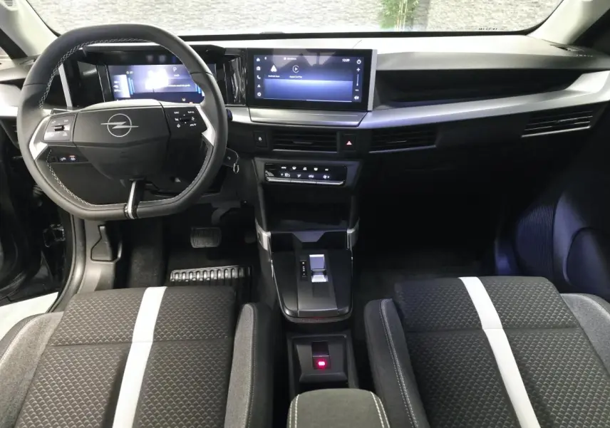 Vue intérieure avant de l’Opel Frontera-e 2025, tableau de bord noir avec écran tactile 10'' et sièges tissu à bande blanche centrale.