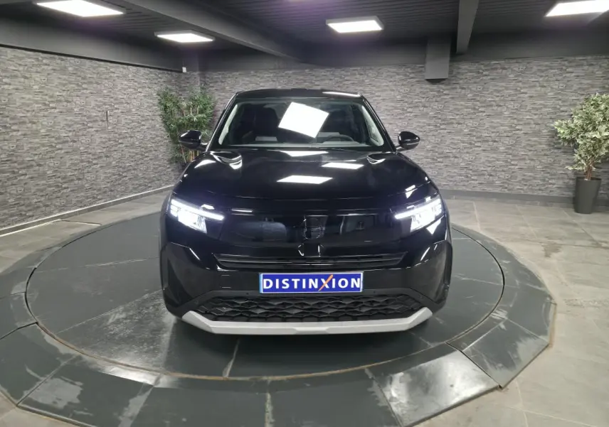 Vue de face d'un Opel Frontera-e noir métallisé avec calandre noire et éclairage LED allumé dans un showroom.