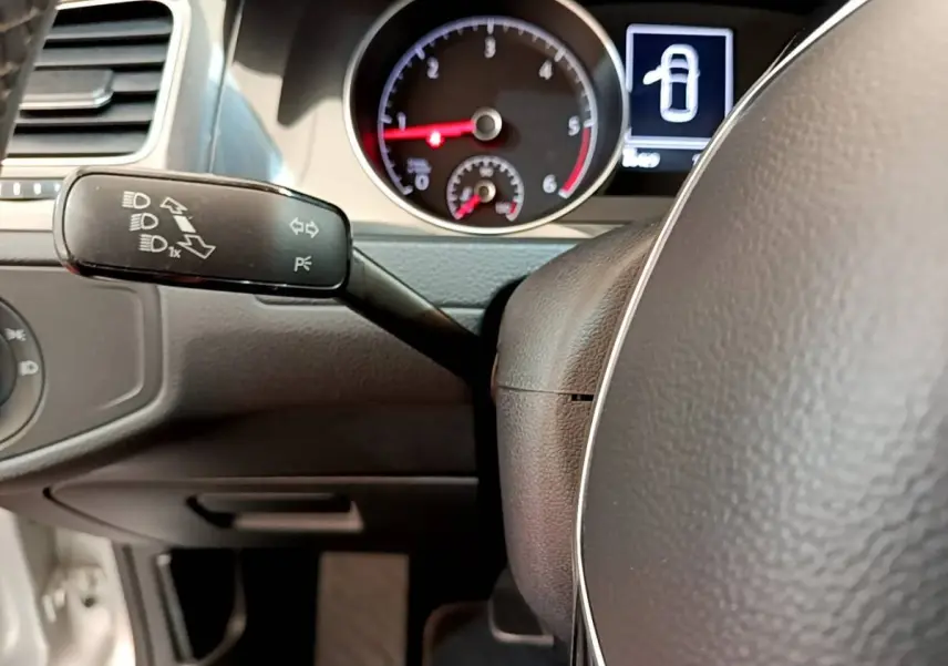 Gros plan sur le volant et le combiné d'instruments du Volkswagen Golf gris clair, avec levier de clignotants visible à gauche.