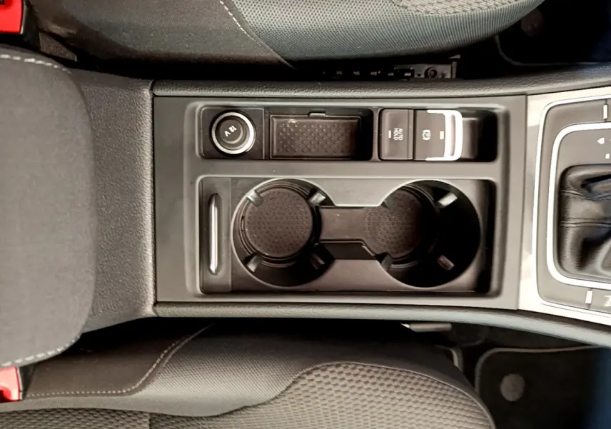 Gros plan sur la console centrale noire de la Volkswagen Golf 1.6 TDI 2019, avec porte-gobelets et bouton frein à main électrique.