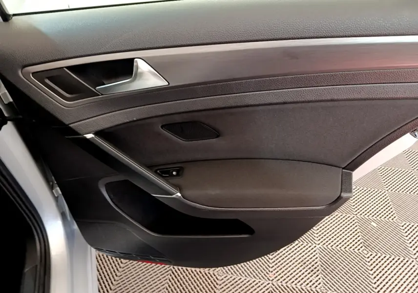 Gros plan sur la porte intérieure côté gauche de la Volkswagen Golf gris clair, avec poignée argentée et garniture noire.