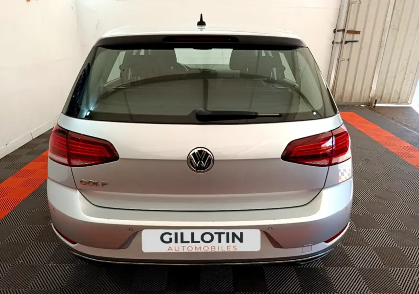 Vue arrière d'une Volkswagen Golf gris clair 2019 garée en intérieur avec logo VW et feux rouges distinctifs.