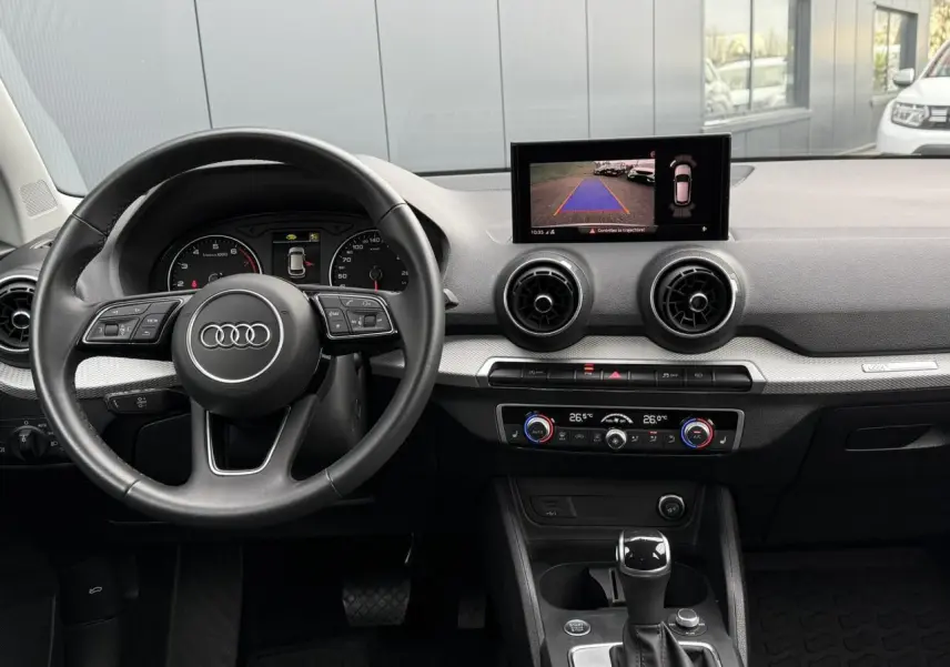 Vue intérieure de l'Audi Q2 35 TFSI 2023 montrant le volant, tableau de bord avec écran caméra de recul et console centrale.