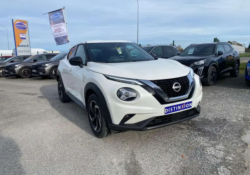 Nissan Juke blanc perle vu en 3/4 avant droit sur parking, avec calandre noire et jantes alliage noires.