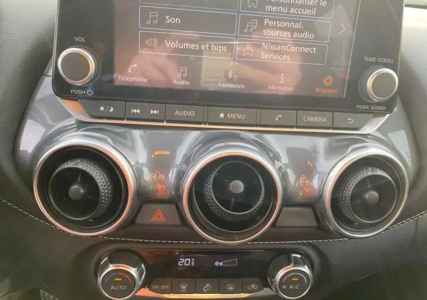 Vue rapprochée du tableau de bord du Nissan Juke blanc perle 2024, mettant en valeur l'écran tactile et les aérateurs ronds chromés.