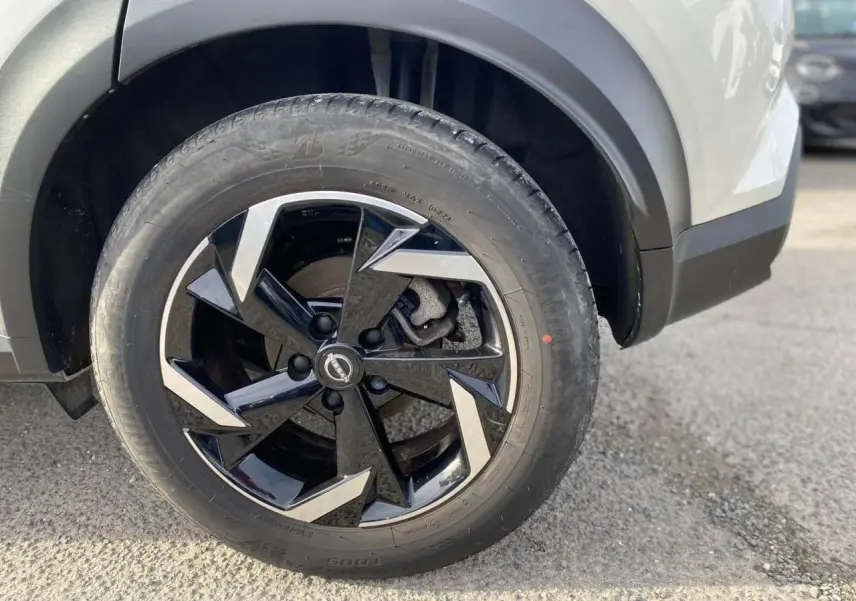 Gros plan sur la roue avant gauche du Nissan Juke blanc perle 2024 avec jante noire et argentée au design moderne.