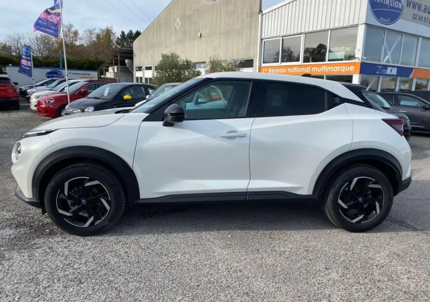 Vue de profil côté gauche d'un Nissan Juke blanc perle 2024 avec jantes noires et détails noirs contrastants.