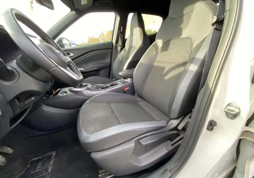 Vue intérieure côté conducteur du Nissan Juke blanc perle 2024, sièges noirs avec motifs géométriques et volant visible.