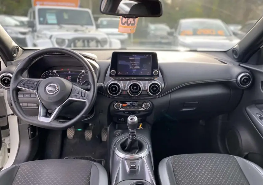 Intérieur du Nissan Juke 2024 blanc perle, vue frontale du tableau de bord avec boîte manuelle et écran tactile central.