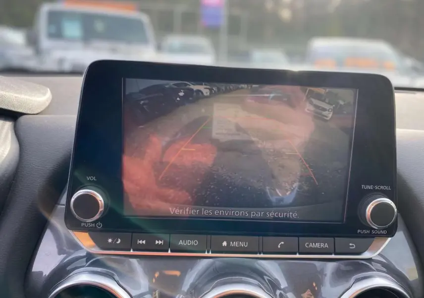 Écran central du Nissan Juke blanc perle 2024 montrant l'image de la caméra de recul avec les lignes de guidage.