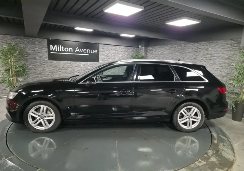 Audi A4 Avant noire vue de profil côté gauche avec jantes aluminium 17 pouces dans un showroom intérieur.