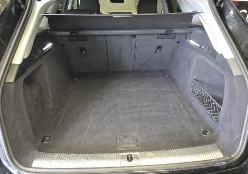 Coffre ouvert vu de l'arrière d'une Audi A4 Avant noire, avec tapis et filet de rangement latéral.
