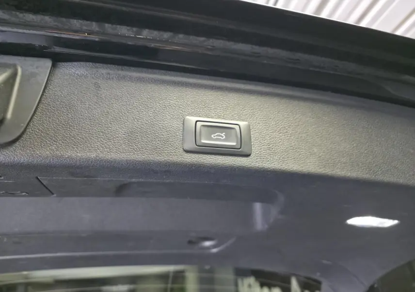Bouton d'ouverture électrique du coffre sur le hayon intérieur d'une Audi A4 Avant noire, vue rapprochée.