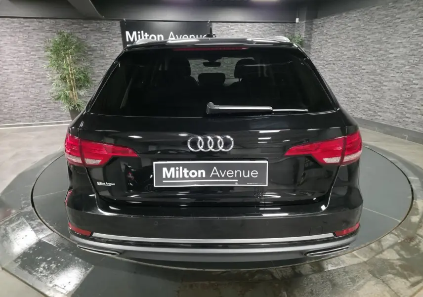 Vue arrière d'une Audi A4 Avant noire avec feux rouges et double sortie d'échappement chromée en intérieur showroom.