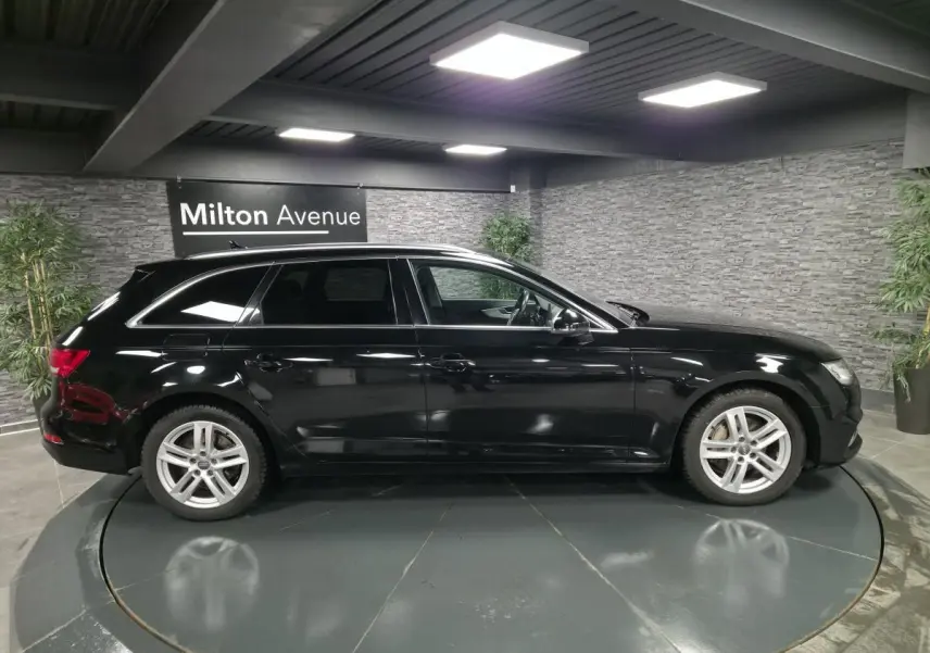 Audi A4 Avant noire vue de profil côté gauche dans un showroom avec jantes aluminium 17 pouces et rétroviseurs noir brillant.