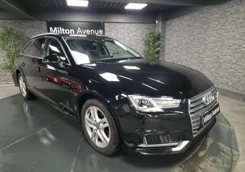 Audi A4 Avant noire vue en 3/4 avant droit dans un showroom avec jantes aluminium 17 pouces et rétroviseurs noirs brillants.