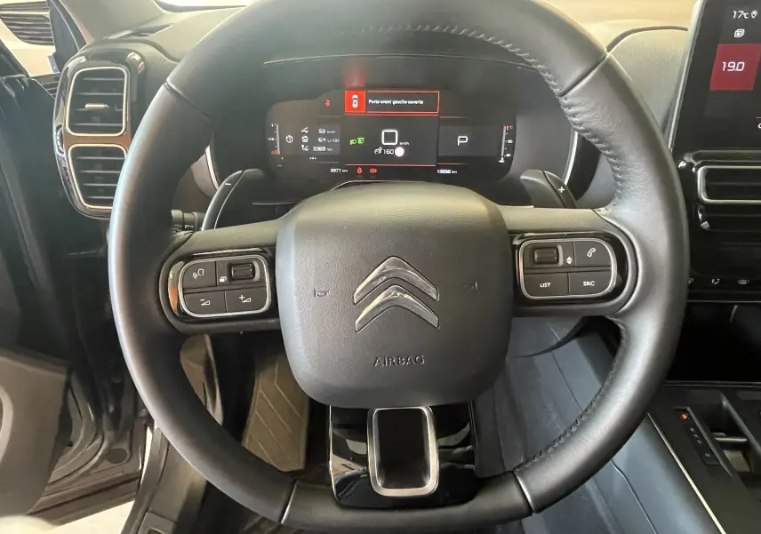 Vue rapprochée du volant cuir du Citroën C5 Aircross hybride 2025, avec commandes intégrées et tableau de bord numérique.