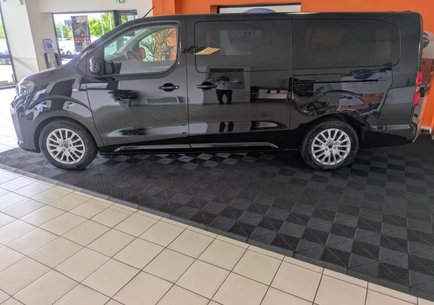 Peugeot Traveller noir vue de profil côté gauche, fourgon spacieux en showroom avec jantes alliage visibles.