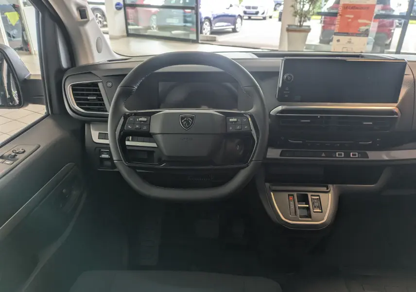 Vue intérieure frontale du Peugeot Traveller noir 2026, mettant en valeur le volant compact et l'écran tactile large du tableau de bord.