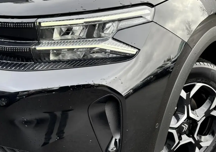 Gros plan sur l’avant droit noir Perla du Citroën C5 Aircross 2025, mettant en valeur le phare LED et la jante alliage 18'' bi-ton.