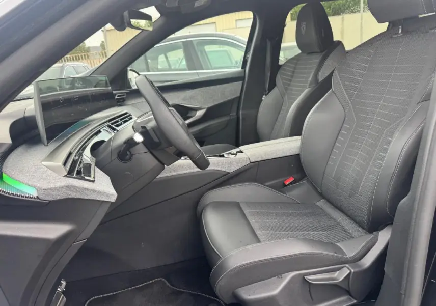 Vue intérieure côté conducteur du Peugeot 5008 Hybrid 145 ch GT 2025, sièges noirs avec accoudoir central et tableau de bord numérique.