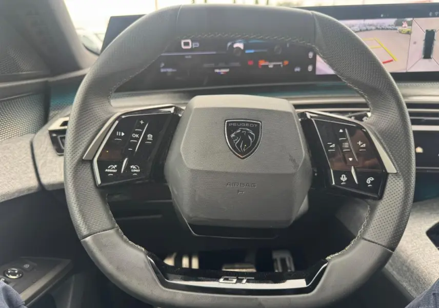 Vue rapprochée du volant noir du Peugeot 5008 Hybrid GT 2025 avec commandes intégrées et tableau de bord numérique.
