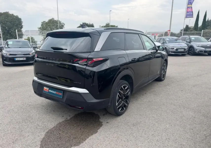Vue 3/4 arrière droite d'un Peugeot 5008 noir 2025 avec jantes alliage 19 pouces et barres de toit visibles.